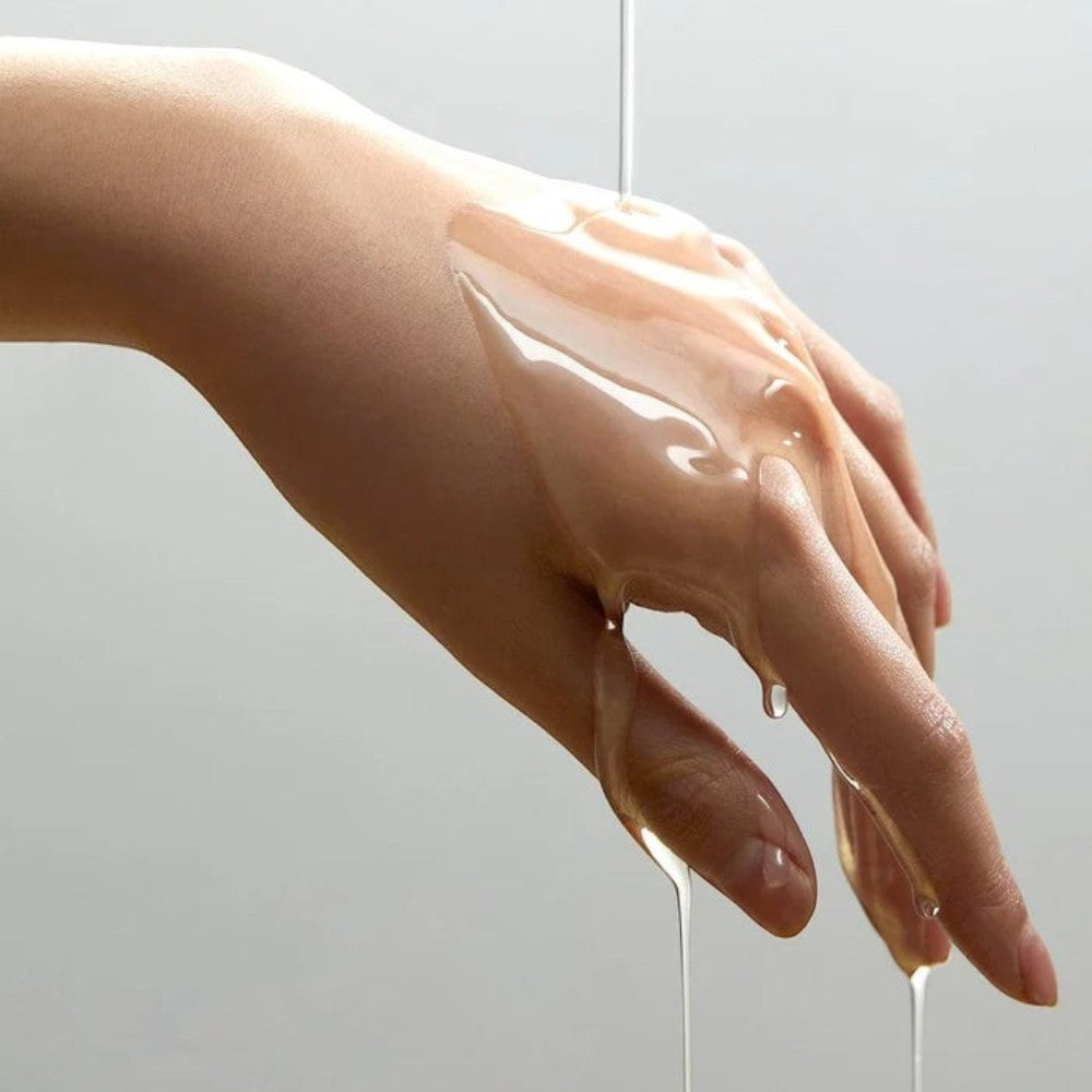 Skin TOGO Anua Heartleaf Pore Control Cleansing Oil texture shown as a clear liquid dripping over a person's hand.