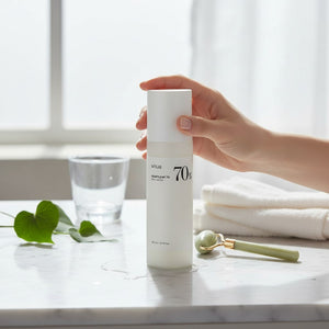 Skin TOGO Anua Heartleaf 70% Daily Lotion bottle held by a hand on a marble surface with a jade roller and towel.