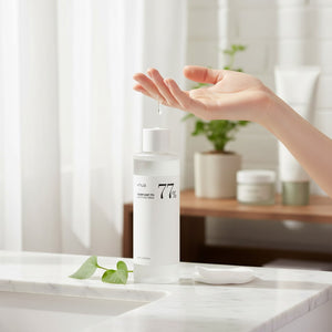Skin TOGO Anua Heartleaf 77 Soothing Toner being poured into a hand on a marble bathroom counter with a plant