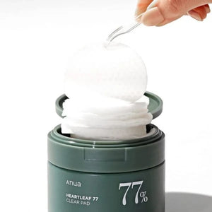 Skin TOGO Anua Heartleaf 77% Clear Pad toner pads being lifted with tweezers from a green jar for acne-prone skin.