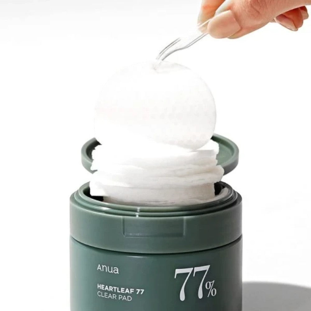 Skin TOGO Anua Heartleaf 77% Clear Pad toner pads being lifted with tweezers from a green jar for acne-prone skin.