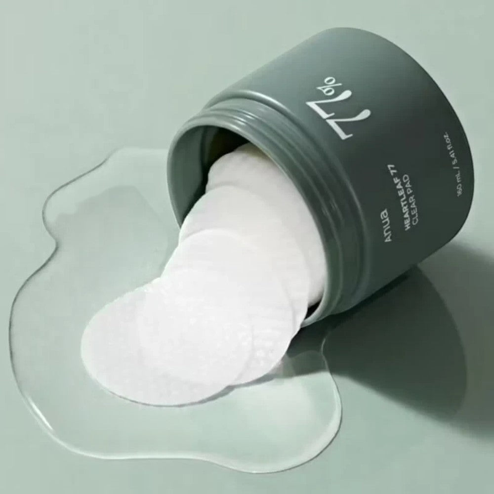 Skin TOGO ANUA Heartleaf 77% Clear Pad toner pads spilling from a green jar with visible essence on a green surface.