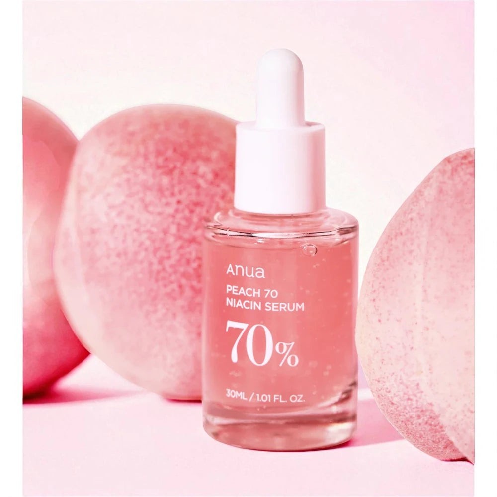 Skin TOGO Anua Peach 70% Niacin Serum in a glass bottle with a dropper, surrounded by fresh peaches on a pink background.