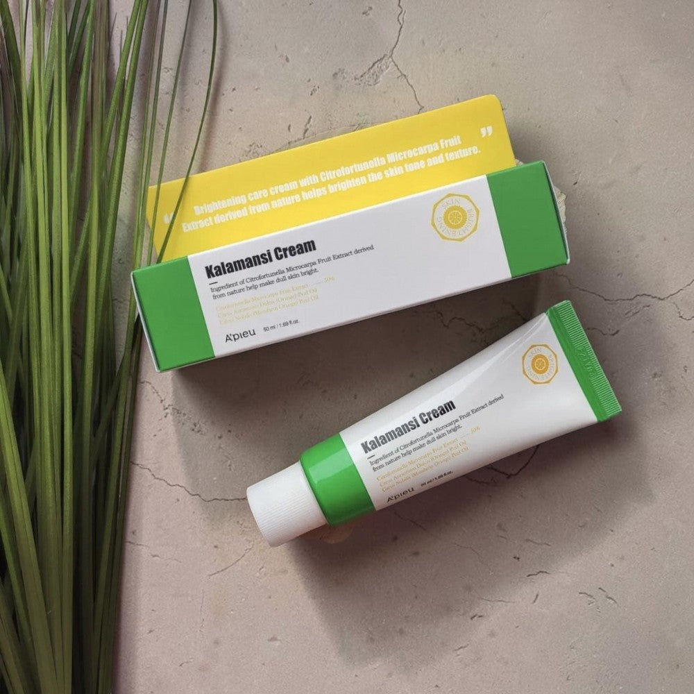 Skin TOGO A'pieu Kalamansi Cream tube and box on a wooden board with green grass, featuring vitamin C brightening.