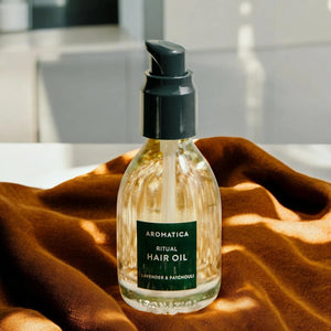 Skin TOGO Aromatica Ritual Hair Oil with lavender and patchouli in a 50ml glass pump bottle on a brown fabric.