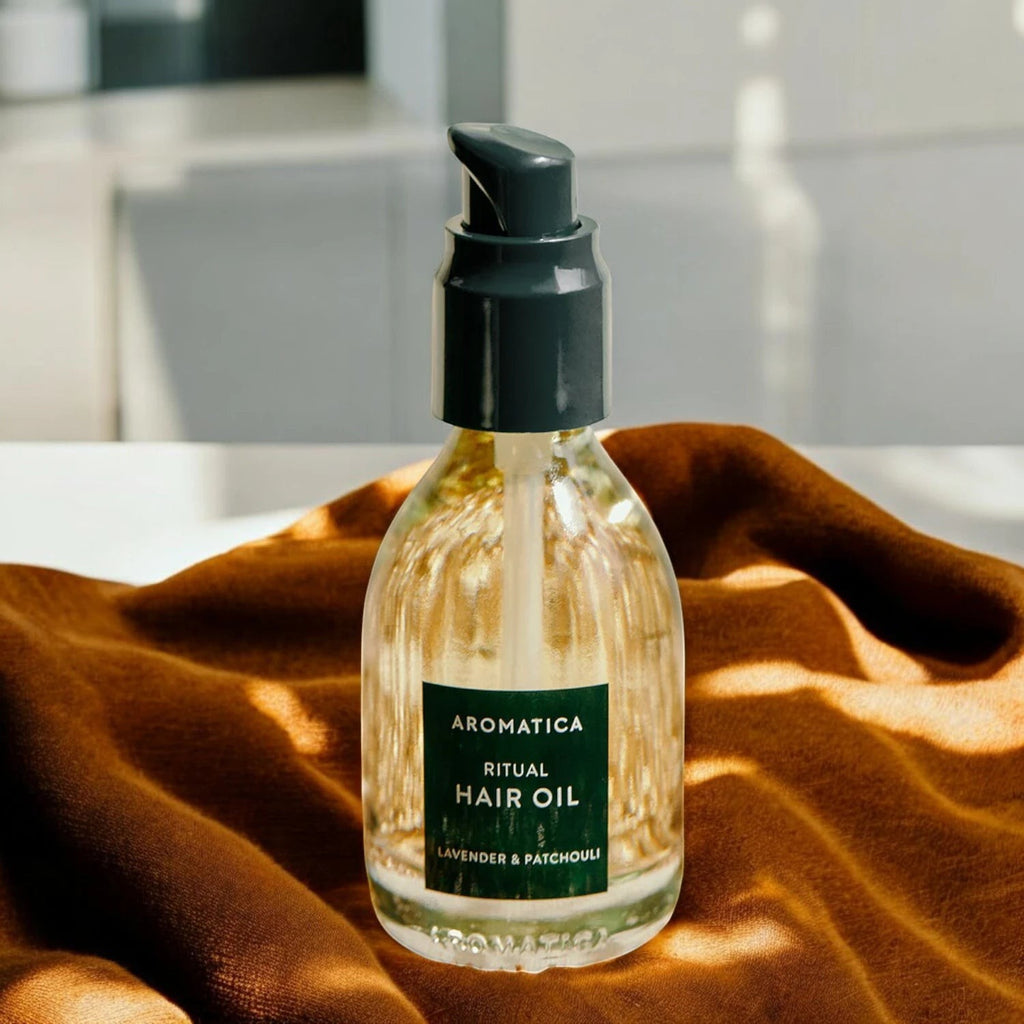 Skin TOGO Aromatica Ritual Hair Oil with lavender and patchouli in a 50ml glass pump bottle on a brown fabric.