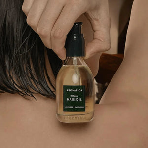 Skin TOGO Aromatica Ritual Hair Oil with lavender and patchouli in a 50ml glass bottle held against a person's back.