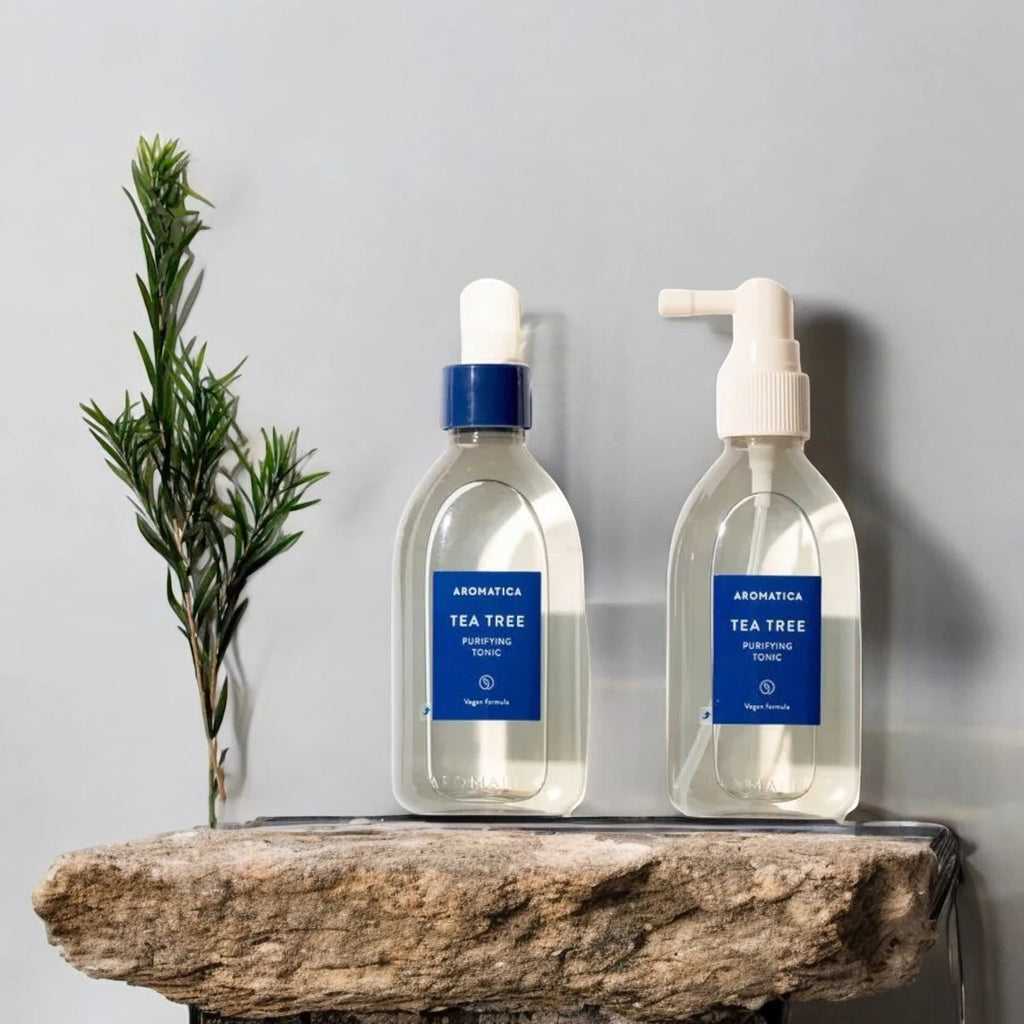 Skin TOGO Aromatica Tea Tree Purifying Tonic bottles with spray and dropper caps on a stone shelf with green foliage.