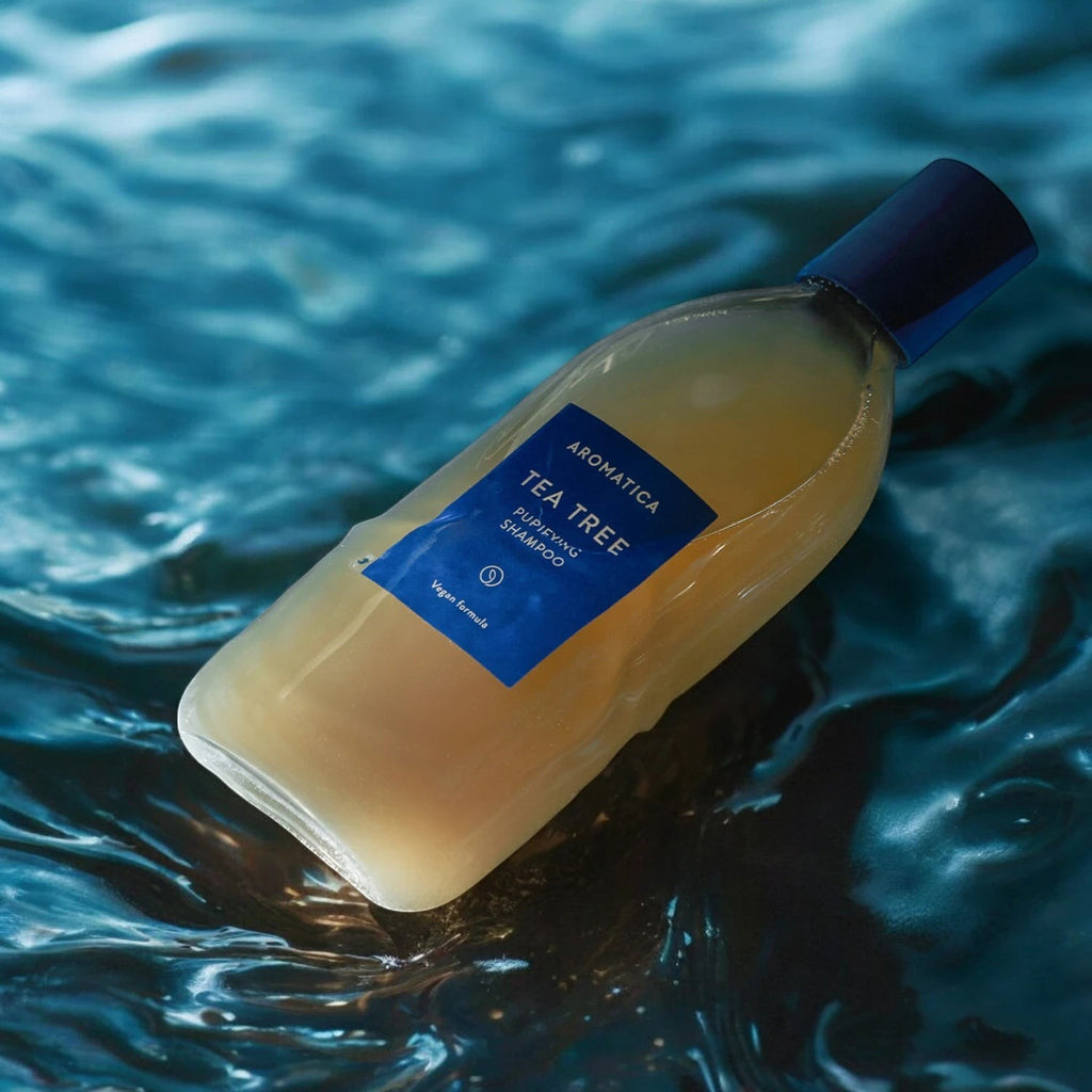Skin TOGO Aromatica Tea Tree Purifying Shampoo in a clear bottle with blue label, resting on a rippling water surface.