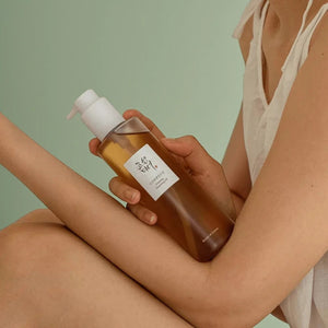 Skin TOGO model holding a bottle of Beauty of Joseon Ginseng Cleansing Oil against a soft green background.