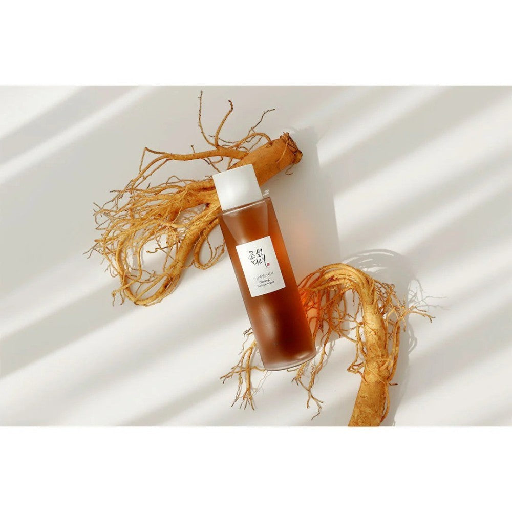 Skin TOGO Beauty of Joseon Ginseng Essence Water in a brown bottle surrounded by fresh ginseng roots on a white surface.