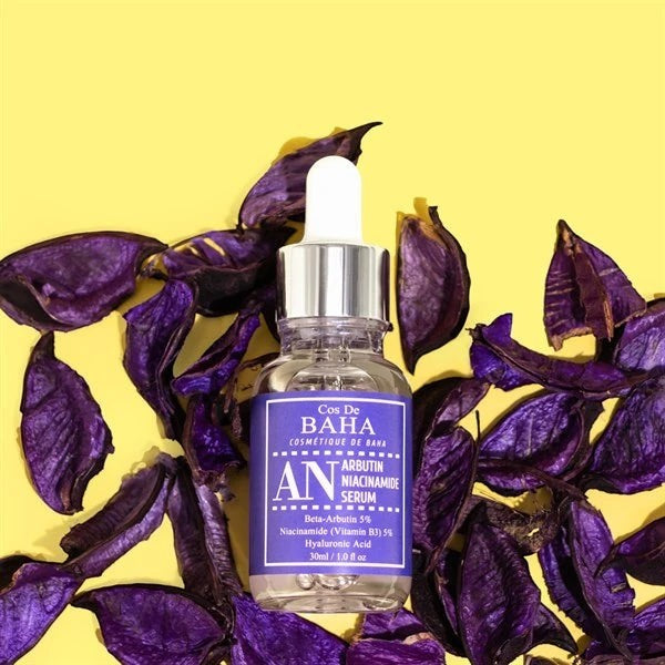 Skin TOGO Cos De BAHA AN Arbutin Niacinamide Serum in a glass dropper bottle surrounded by purple dried flower petals.