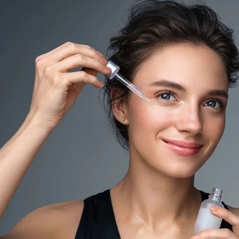 Skin TOGO model applying Cos De BAHA P.M.A Peptide Serum with a dropper to her face for anti-aging skin care.