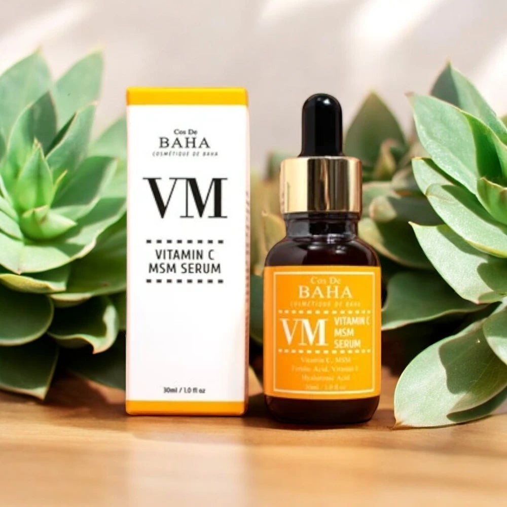 Skin TOGO Cos De BAHA VM Vitamin C MSM serum bottle and box with yellow labels, surrounded by green succulent plants.