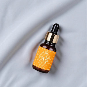 Skin TOGO Cos De BAHA VM Vitamin C MSM serum in an amber glass dropper bottle on a soft grey fabric background.