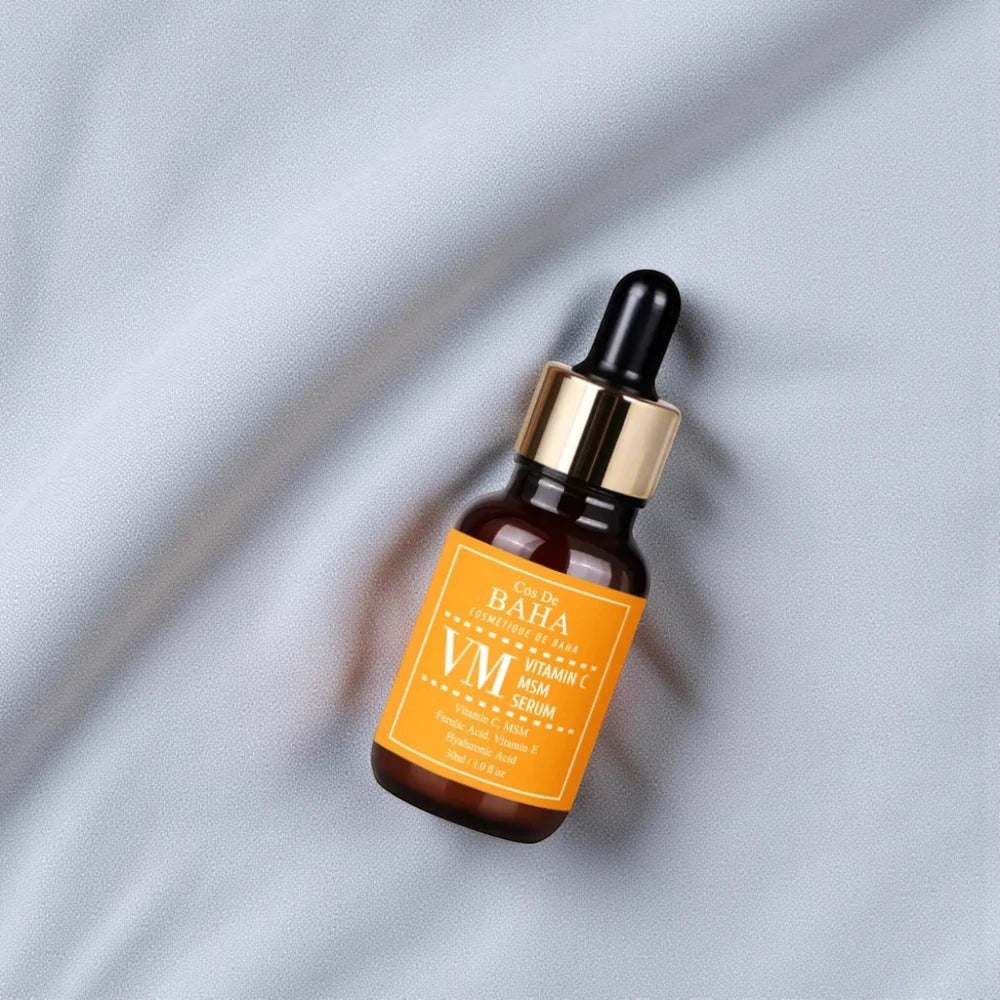 Skin TOGO Cos De BAHA VM Vitamin C MSM serum in an amber glass dropper bottle on a soft grey fabric background.