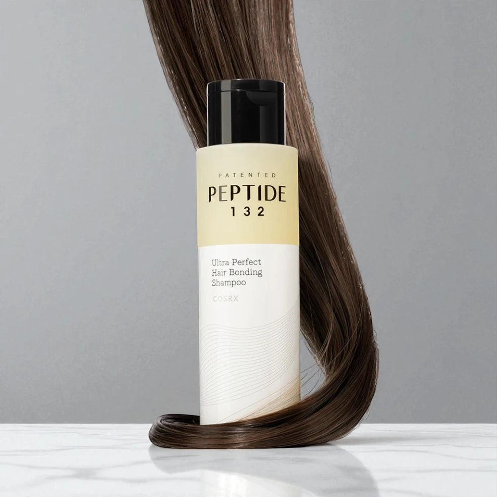 Skin TOGO COSRX Peptide-132 Ultra Perfect Hair Bonding Shampoo bottle with a lock of hair on a marble surface.