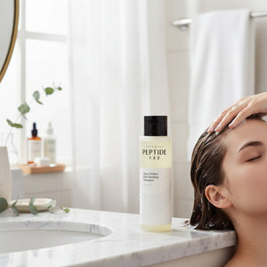 Skin TOGO COSRX Peptide-132 bonding shampoo bottle on a marble bathroom counter with a person washing their hair.
