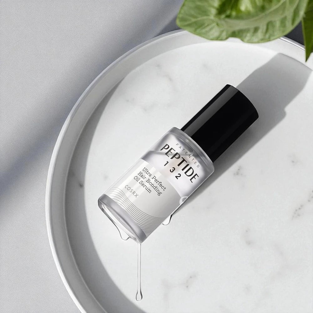 Skin TOGO COSRX Peptide-132 hair bonding oil serum in a clear bottle on a white marble tray with a green leaf.