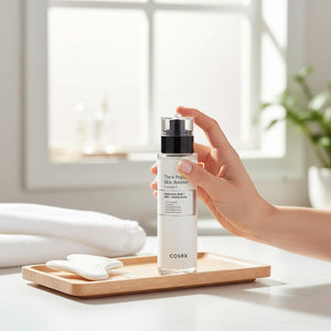 Skin TOGO COSRX The 6 Peptide Skin Booster serum bottle held by a hand on a wooden tray with a gua sha tool.