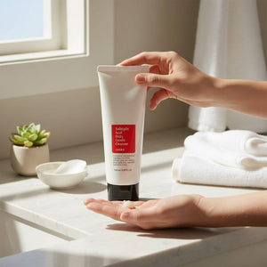 Skin TOGO Cosrx Salicylic Acid Daily Gentle Cleanser in a white tube held over a hand in a bright bathroom setting.