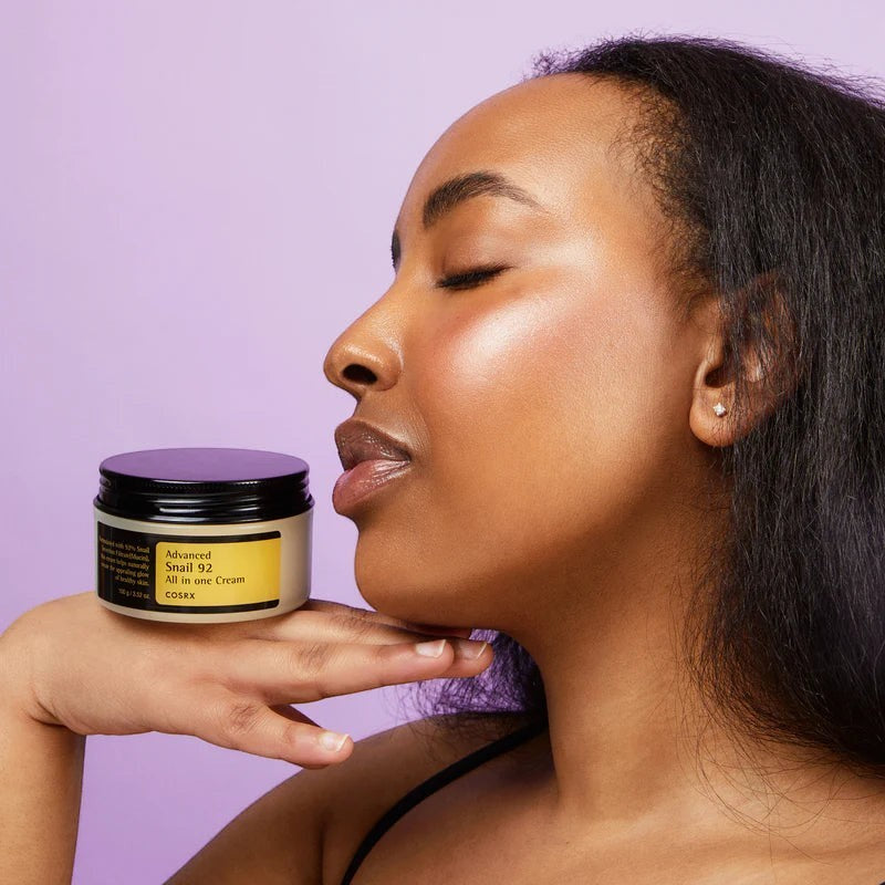 Skin TOGO model holding a jar of Cosrx Advanced Snail 92 All In One Cream against a soft purple background