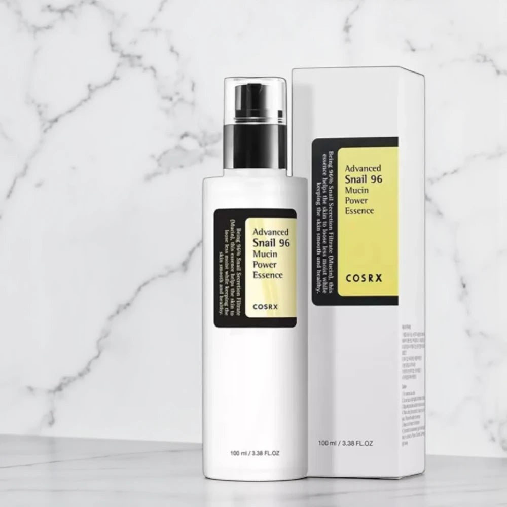 Skin TOGO Cosrx Advanced Snail 96 Mucin Power Essence bottle and its yellow and white packaging box on marble surface.