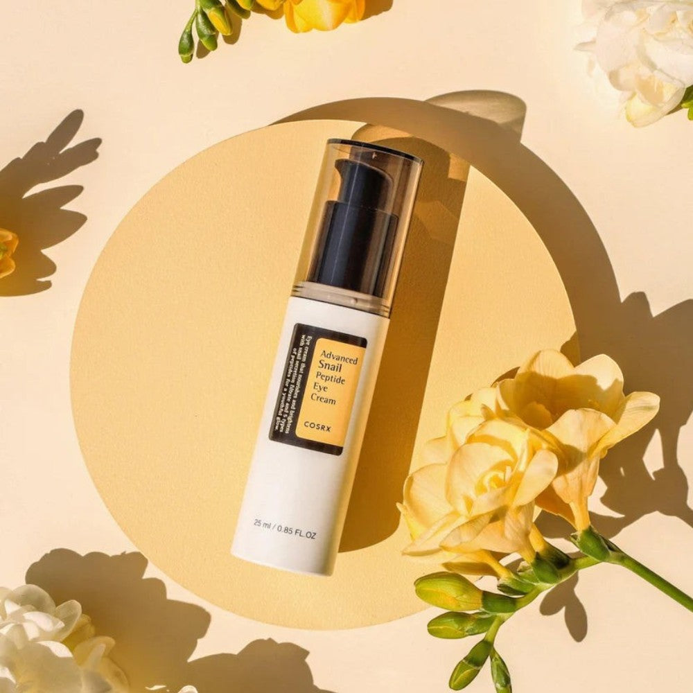 Skin TOGO Cosrx Advanced Snail Peptide Eye Cream in a white pump bottle on a yellow circular platform with flowers