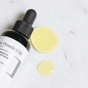 Skin TOGO COSRX The Vitamin C 13 serum bottle with a dropper and two golden yellow serum drops on a marble surface.