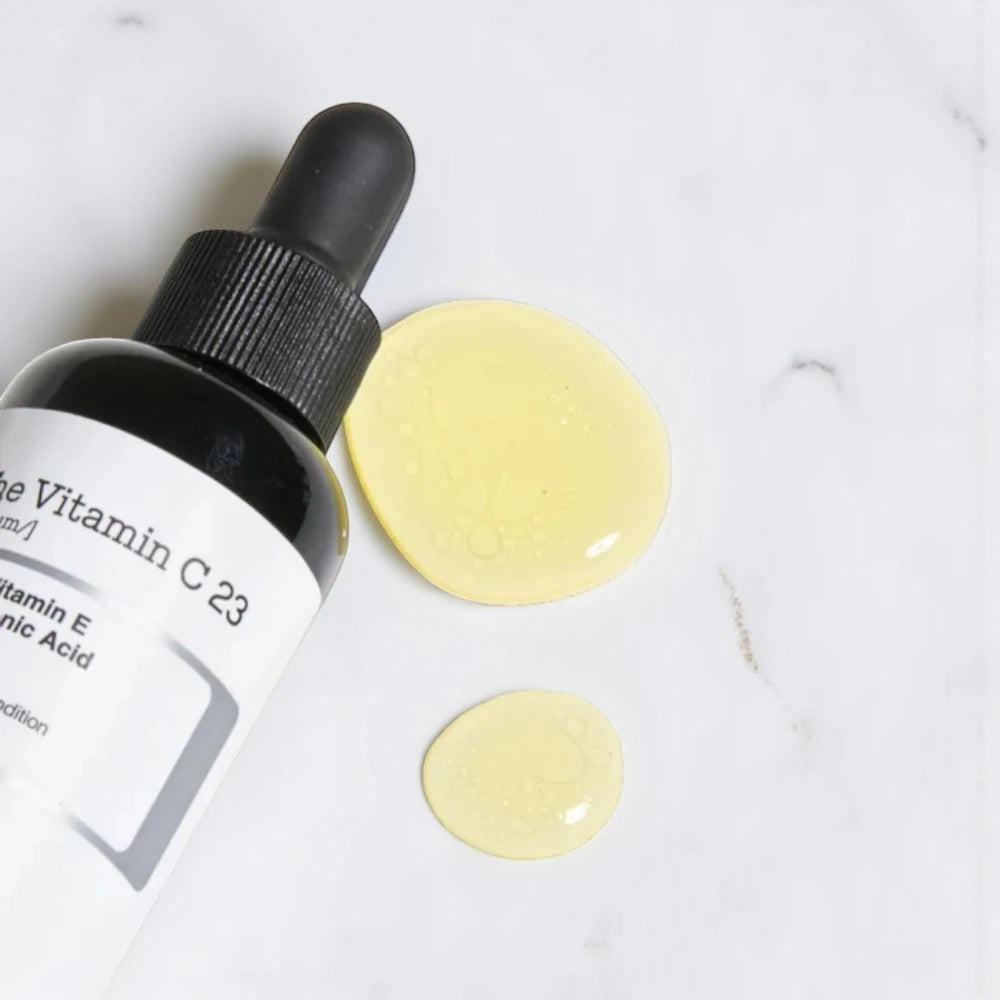 Skin TOGO COSRX The Vitamin C 13 serum bottle with a dropper and two golden yellow serum drops on a marble surface.