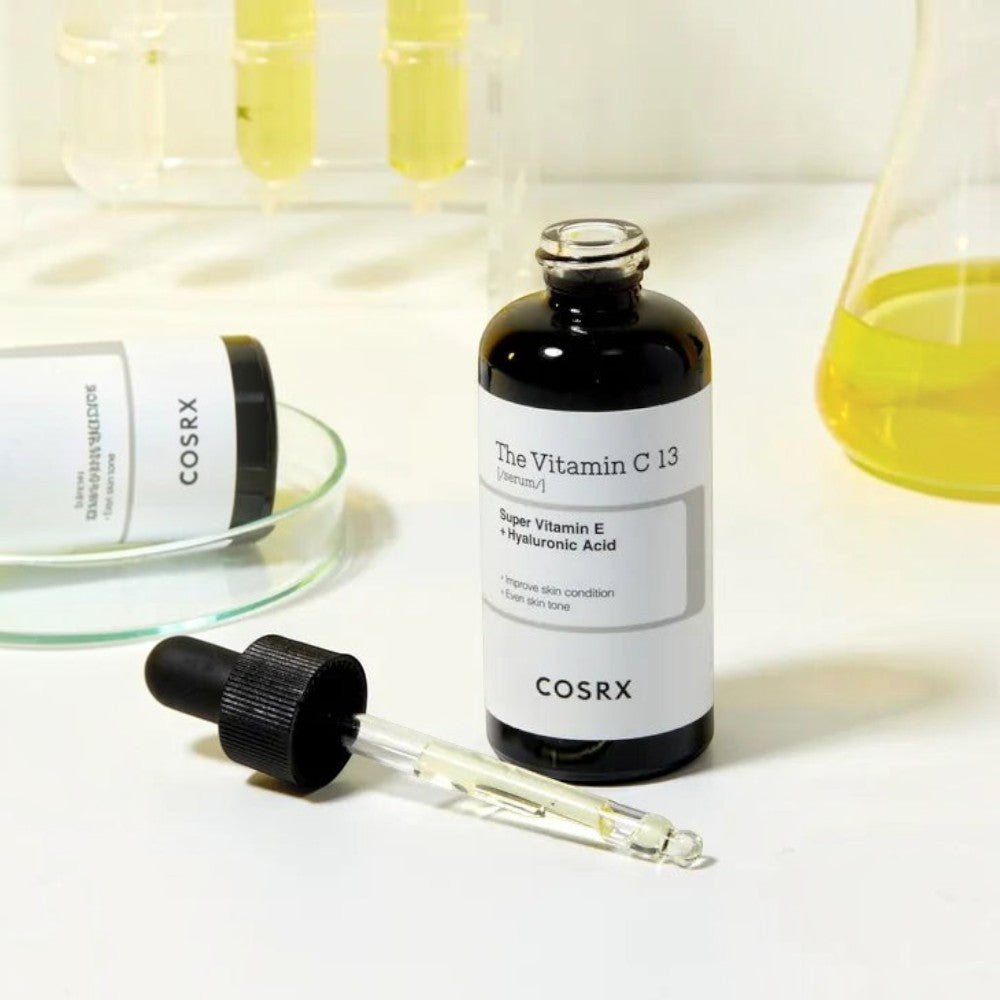 Skin TOGO COSRX The Vitamin C 13 Serum bottle with dropper in a laboratory setting with beakers and test tubes.