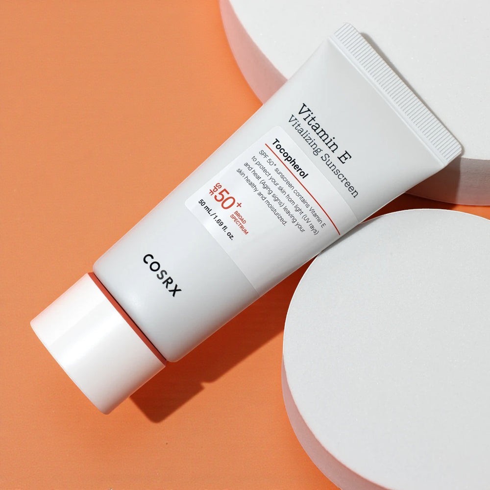 Skin TOGO COSRX Vitamin E Vitalizing Sunscreen SPF 50+ in a white 50ml tube on a minimalist orange and white display.
