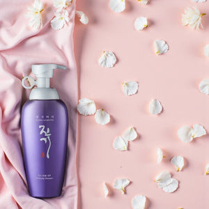 Skin TOGO Daeng Gi Meo Ri Vitalizing Shampoo in a purple bottle on a pink cloth with white flower petals.
