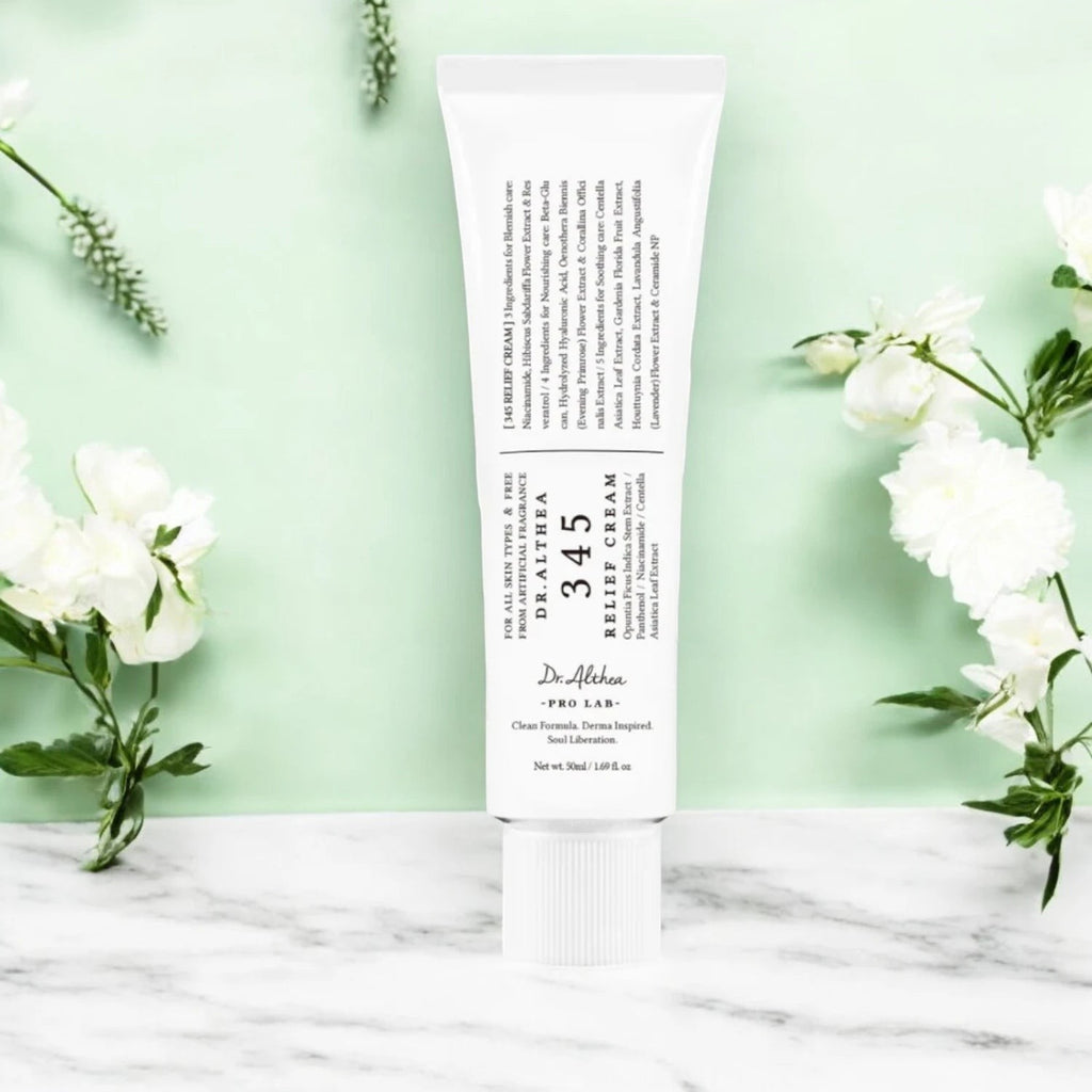 Skin TOGO Dr.Althea 345 Relief Cream in a white tube on a marble surface with white flowers against a green background