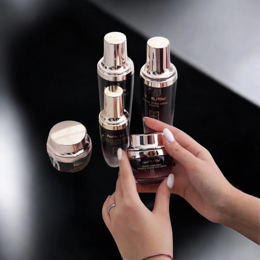 Skin TOGO Farmstay Grape Stem Cell eye cream jar held in hands with matching skincare bottles on a black background.