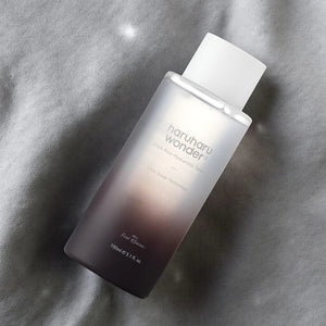 Skin TOGO Haruharu WONDER Black Rice Hyaluronic Toner in a gradient frosted bottle on a grey fabric background.
