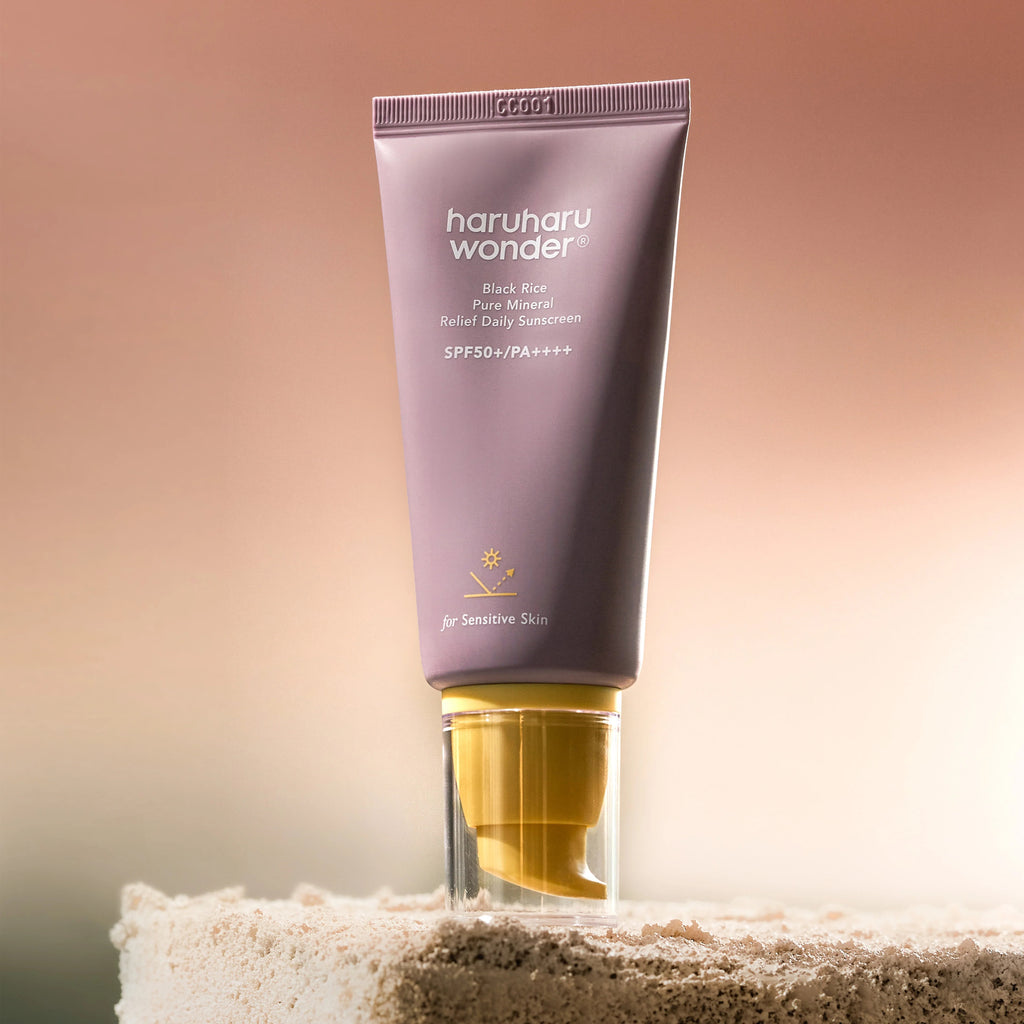 Skin TOGO Haruharu WONDER Black Rice mineral sunscreen in a mauve tube with a yellow cap on a textured stone base.