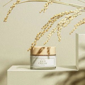 Skin TOGO I'm from Rice Cream in a glass jar with a beige lid, displayed on a pedestal with dried rice stalks.