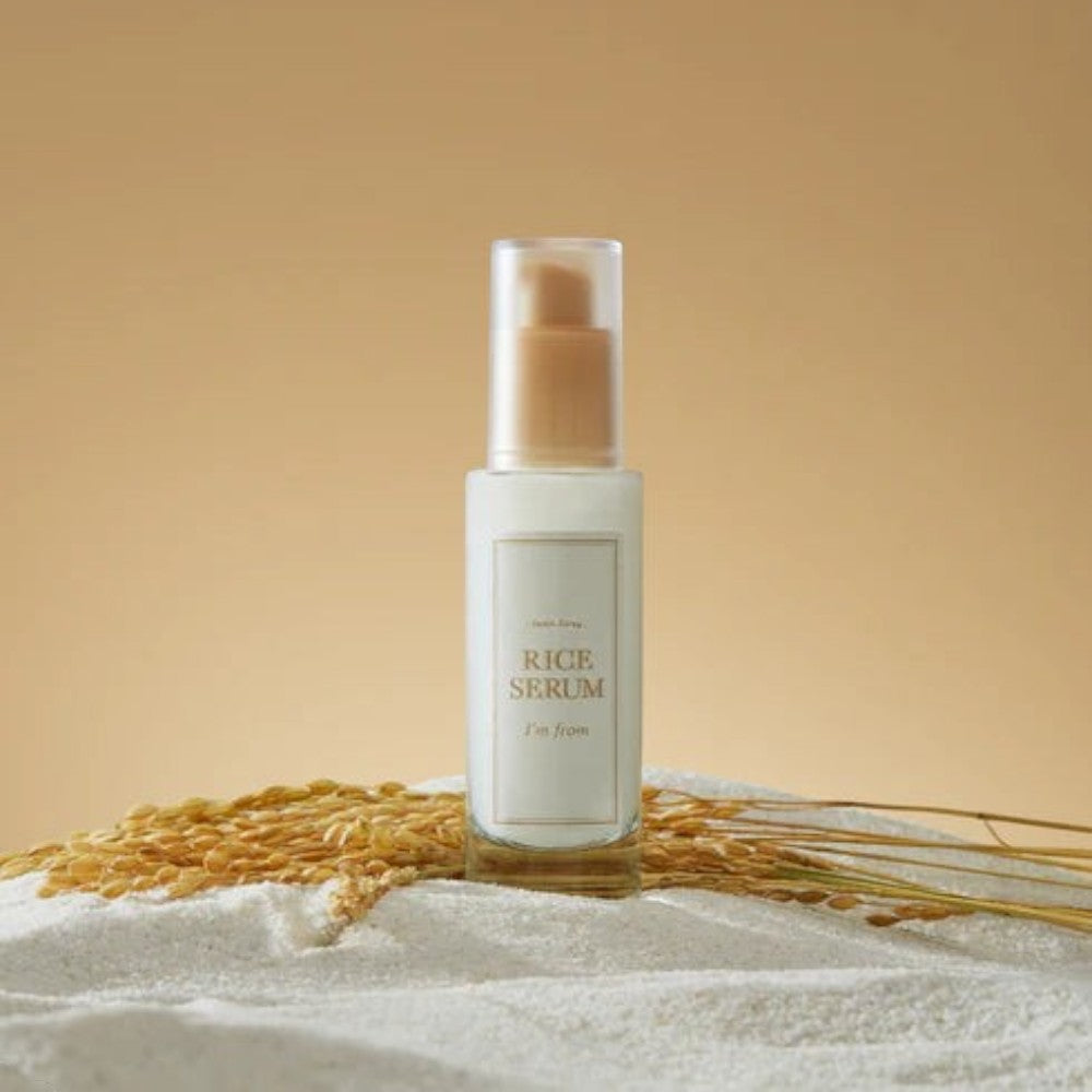 Skin TOGO I'm from Rice Serum in a glass bottle with a pump, surrounded by rice grains on a beige background.