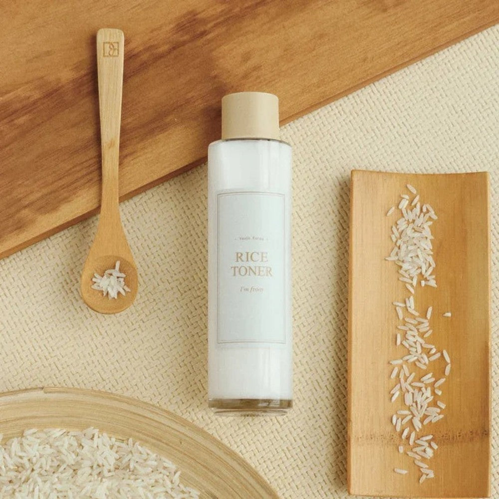 Skin TOGO I'm from Rice Toner in a clear bottle with milky liquid, displayed with a wooden spoon and raw rice grains.