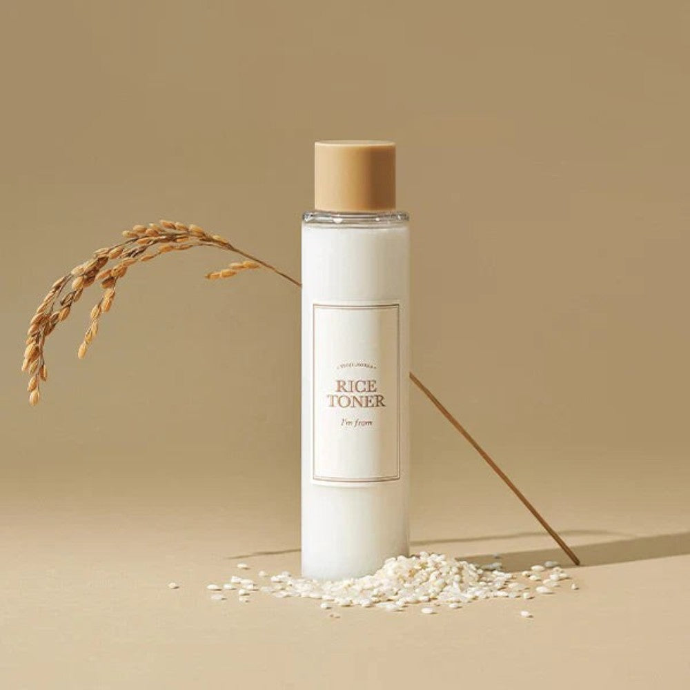 Skin TOGO I'm from Rice Toner bottle with milky texture, displayed with rice grains and a rice stalk on a beige background