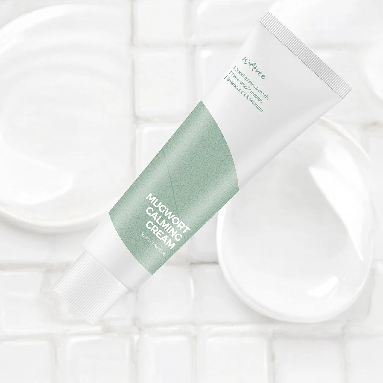 Skin TOGO Isntree Mugwort Calming Cream in a white and sage green tube on a white tiled background.