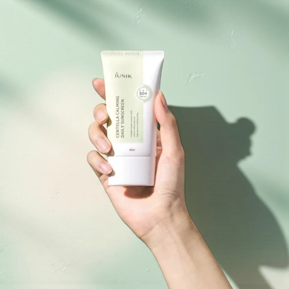 Skin TOGO iUNIK Centella Calming Sun Cream in a hand against a soft green background with natural light shadows.