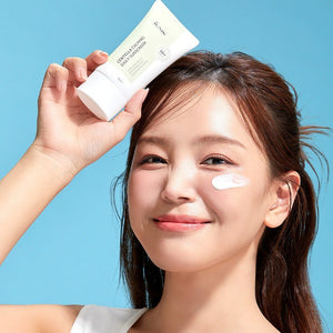 Skin TOGO model holding iUNIK Centella Calming Sun Cream with SPF50+ protection on her cheek against a blue background