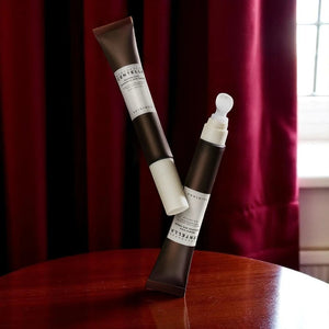 Skin TOGO Madagascar Centella Probio-Cica Bakuchiol Eye Cream tubes balanced on a wooden table against red curtains.