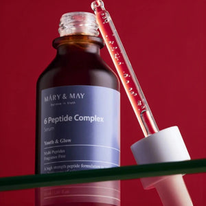 Skin TOGO Mary & May 6 Peptide Complex anti-aging serum in a brown glass bottle with a glass dropper on red background