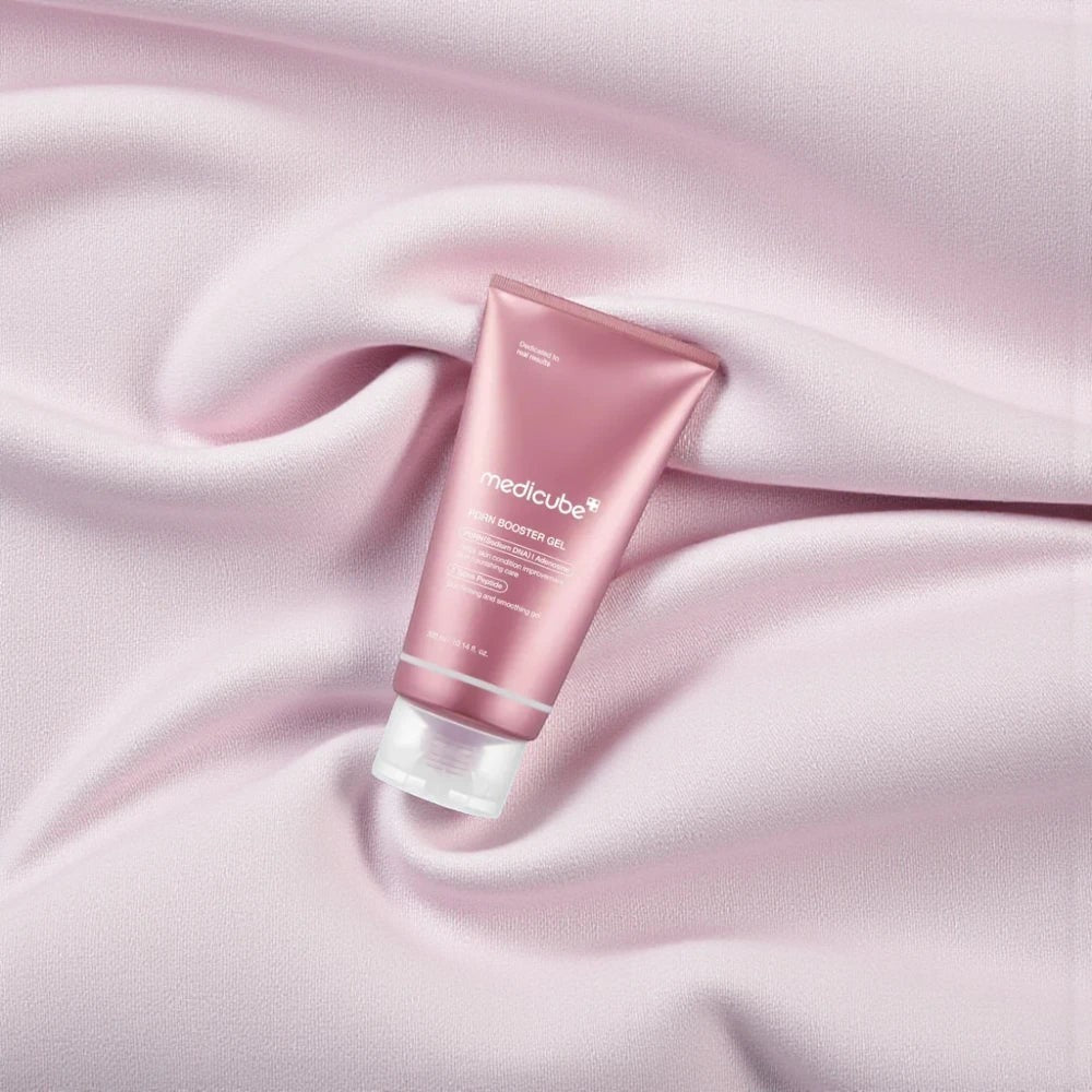 Skin TOGO Medicube PDRN Booster Gel in a pink tube resting on soft, draped light pink fabric.