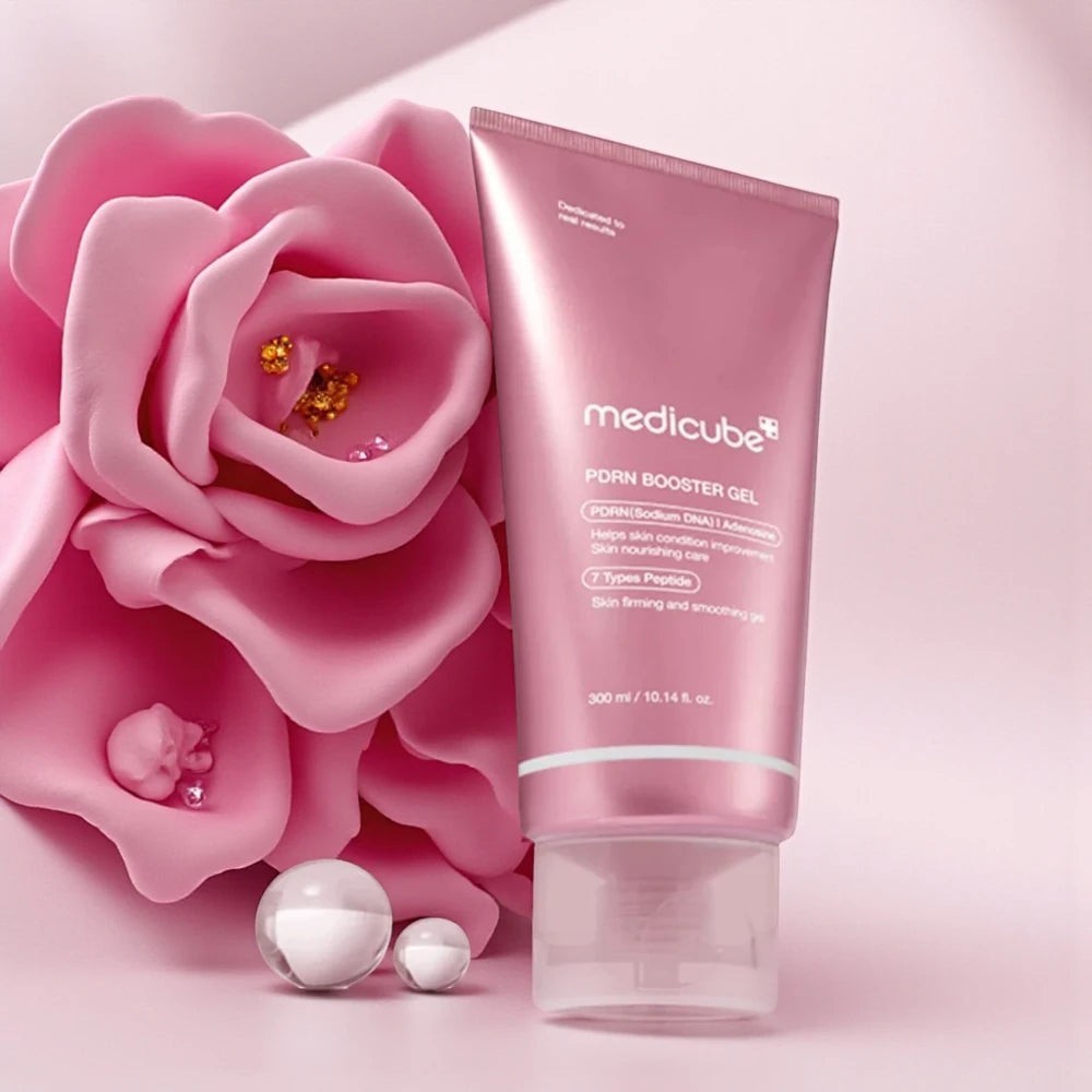Skin TOGO Medicube PDRN Booster Gel in a pink tube next to a large pink flower and decorative pearls.
