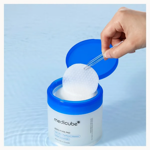Skin TOGO Medicube Zero Pore Pad jar with blue lid, showing a hand using tweezers to lift a textured exfoliating pad.