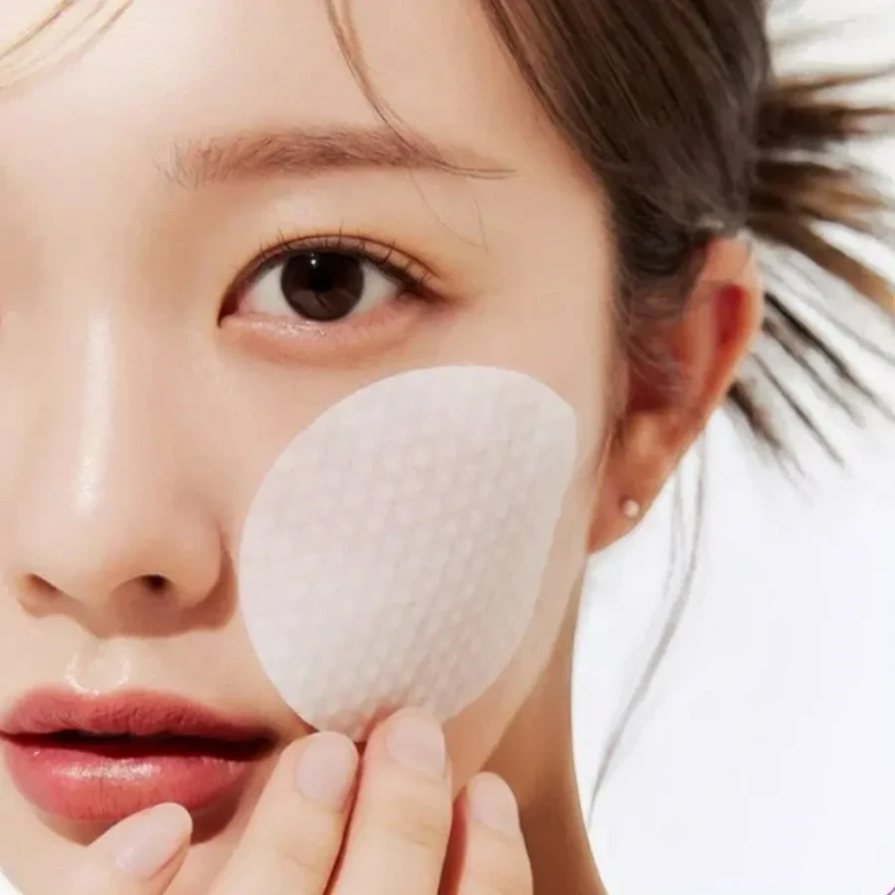 Skin TOGO Medicube Zero Pore Pad being applied to a woman's cheek for gentle exfoliation and pore refinement.